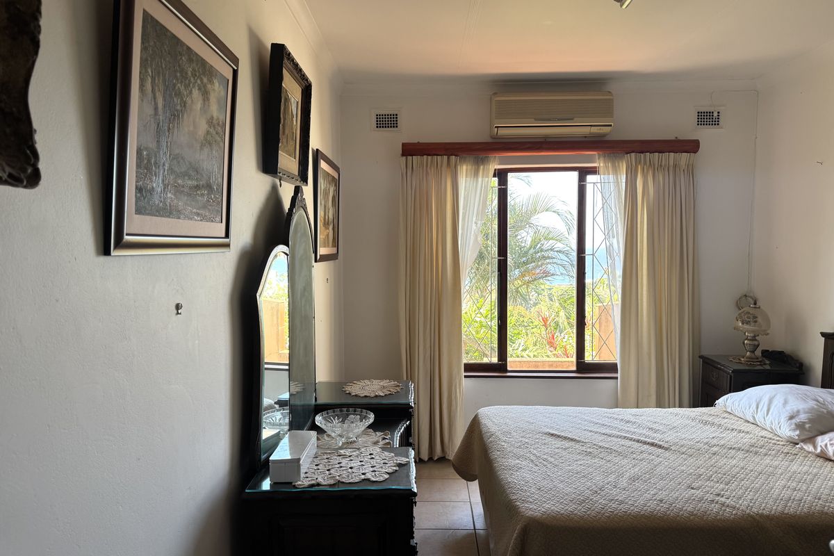 A bedroom featuring tiled flooring, a split-system air conditioner, and a window with security gate, offering natural light and a view.