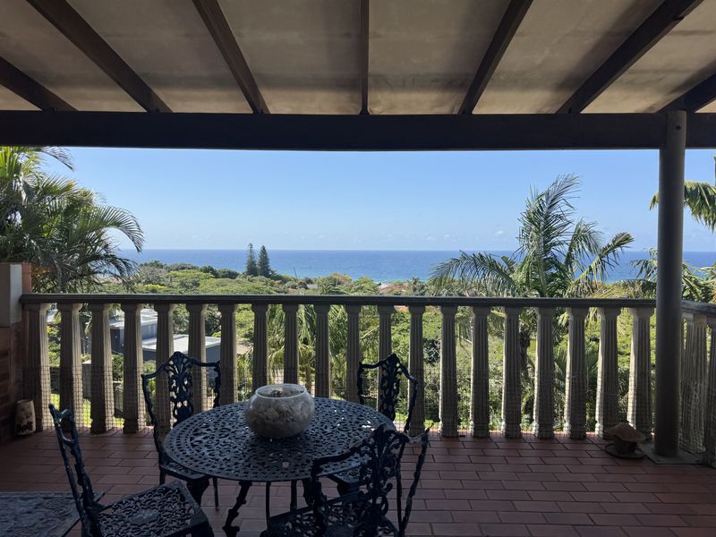 A spacious covered patio featuring a classic balustrade and tiled flooring, offering expansive elevated views of the surrounding landscape and ocean.