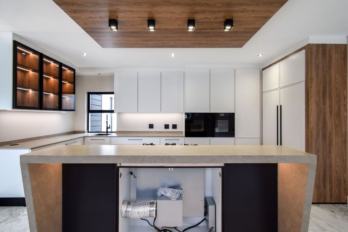 Modern kitchen featuring sleek white cabinetry, integrated appliances, stone countertops, and a wood-paneled ceiling detail with recessed lighting.