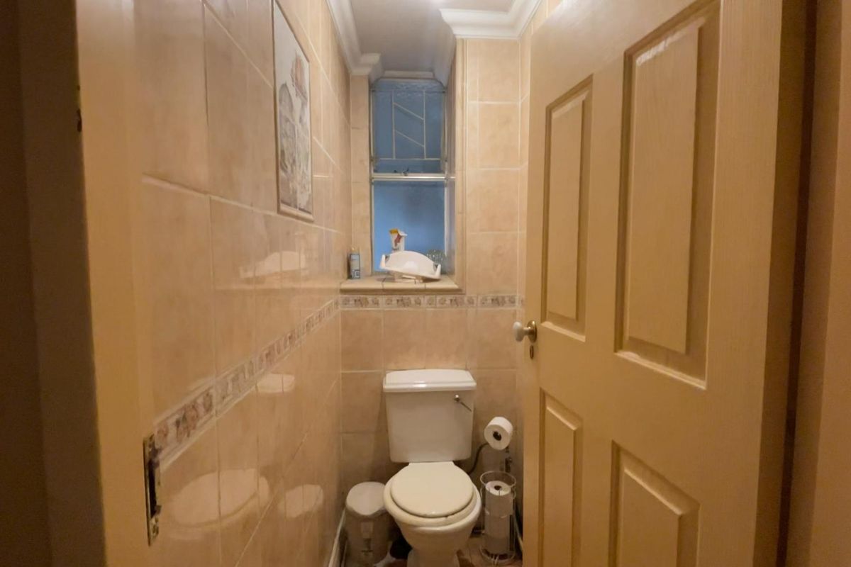 A compact guest bathroom featuring floor-to-ceiling wall tiles, a standard toilet, and a small window for natural light.