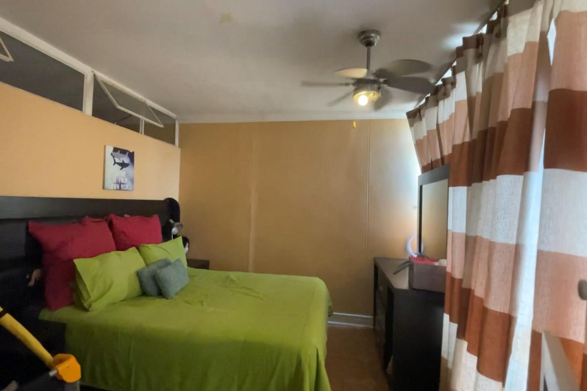 A bedroom featuring a ceiling fan, transom windows, and neutral wall tones, providing a functional sleeping space.