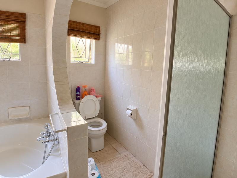A functional bathroom featuring a built-in bathtub, a separate shower enclosure, and a toilet, finished with neutral wall and floor tiles.