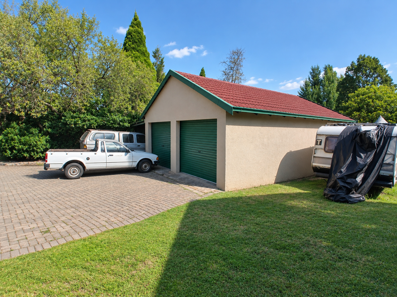 A detached double garage featuring a tiled roof and green roller doors, situated on a paved driveway with surrounding garden space.