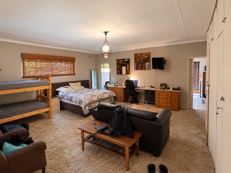 Spacious bedroom featuring built-in cupboards, carpeted flooring, and bamboo blinds, offering a versatile layout with ample storage space.
