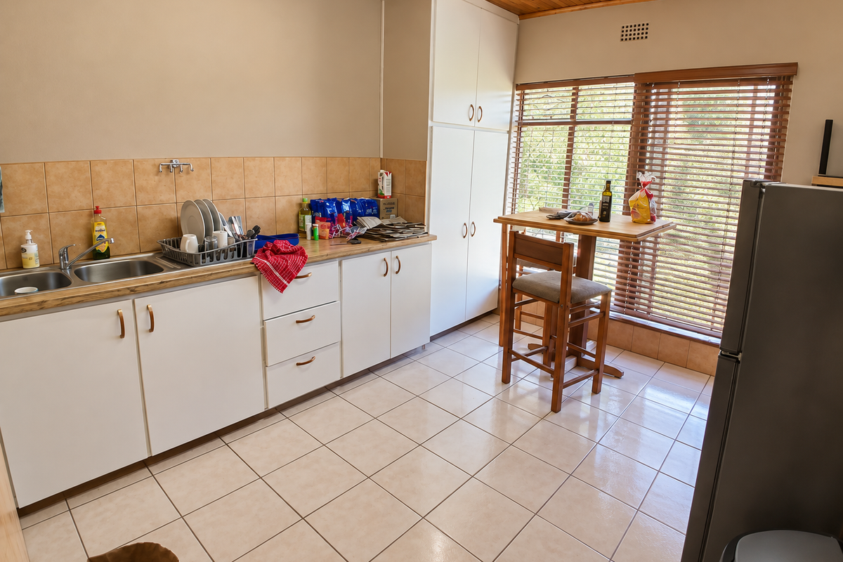 A functional kitchen featuring white cabinetry, tiled backsplash, double basin sink, and tiled flooring with a timber ceiling and natural light.