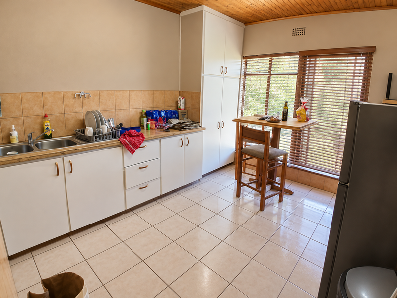 A functional kitchen featuring white cabinetry, tiled backsplash, double basin sink, and tiled flooring with a timber ceiling and natural light.