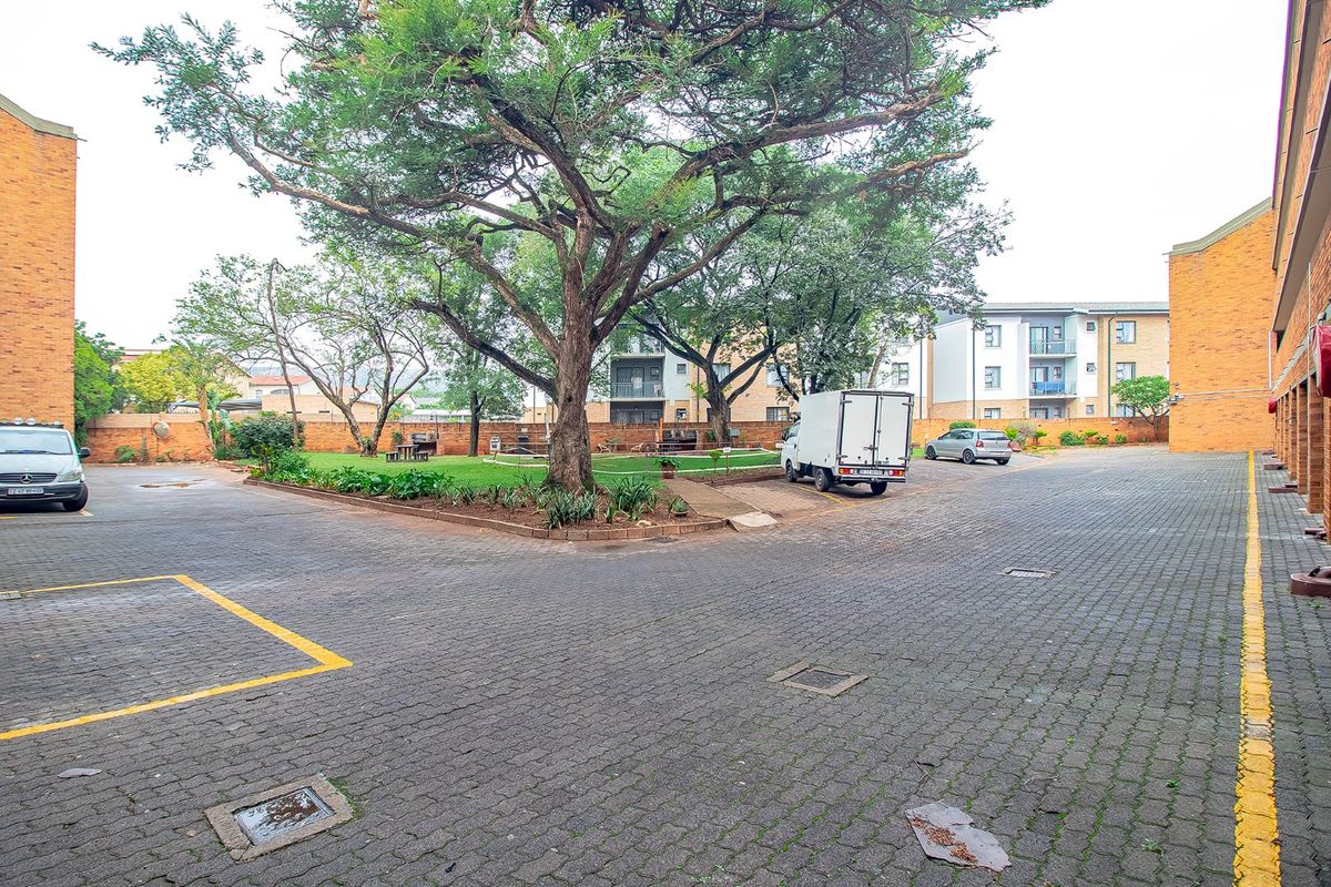 A view of the apartment complex courtyard featuring paved parking areas, mature trees, and landscaped garden beds.
