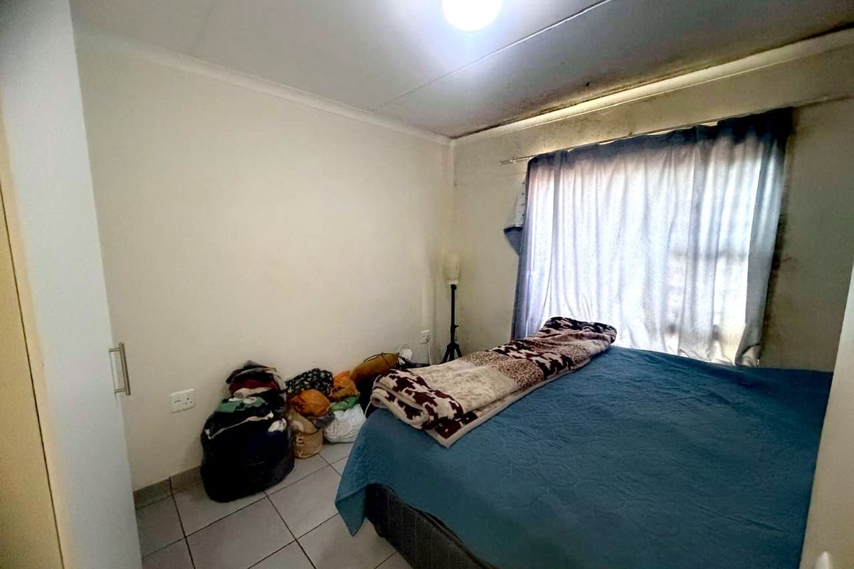 A bedroom featuring tiled flooring, a built-in cupboard, and a window with curtaining.