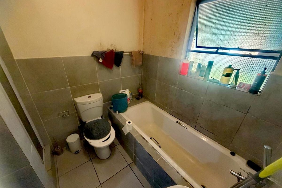 A compact bathroom featuring a standard bathtub, toilet, and tiled wall surrounds, currently requiring significant cosmetic updates and maintenance.