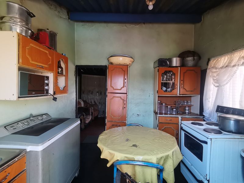 A dated kitchen featuring original cabinetry, an electric stove, and built-in microwave, requiring cosmetic updates and wall repairs to modernize the space.