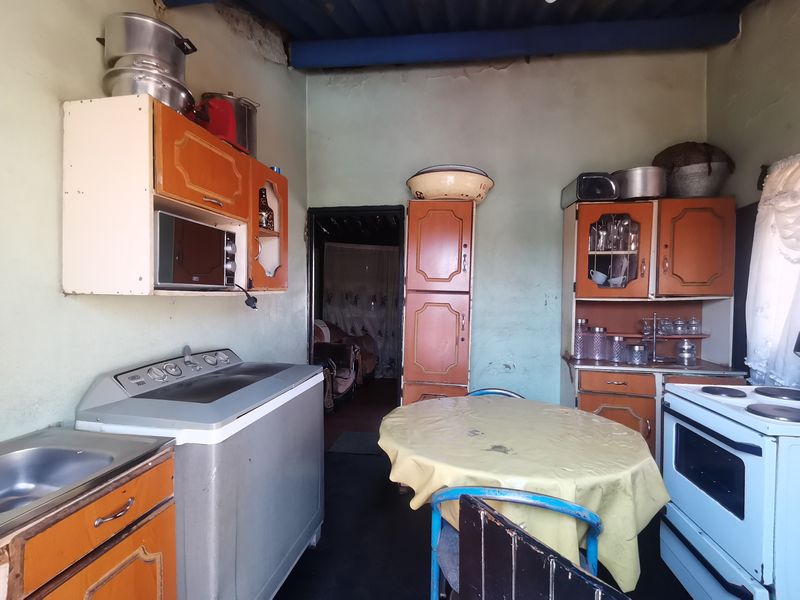 A dated kitchen featuring original built-in cabinetry, a sink, and a freestanding stove, requiring significant cosmetic updates and surface repairs.