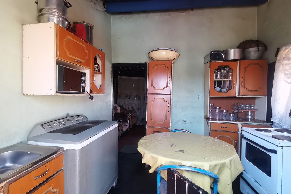 A dated kitchen featuring original built-in cabinetry, a sink, and a freestanding stove, requiring significant cosmetic updates and surface repairs.