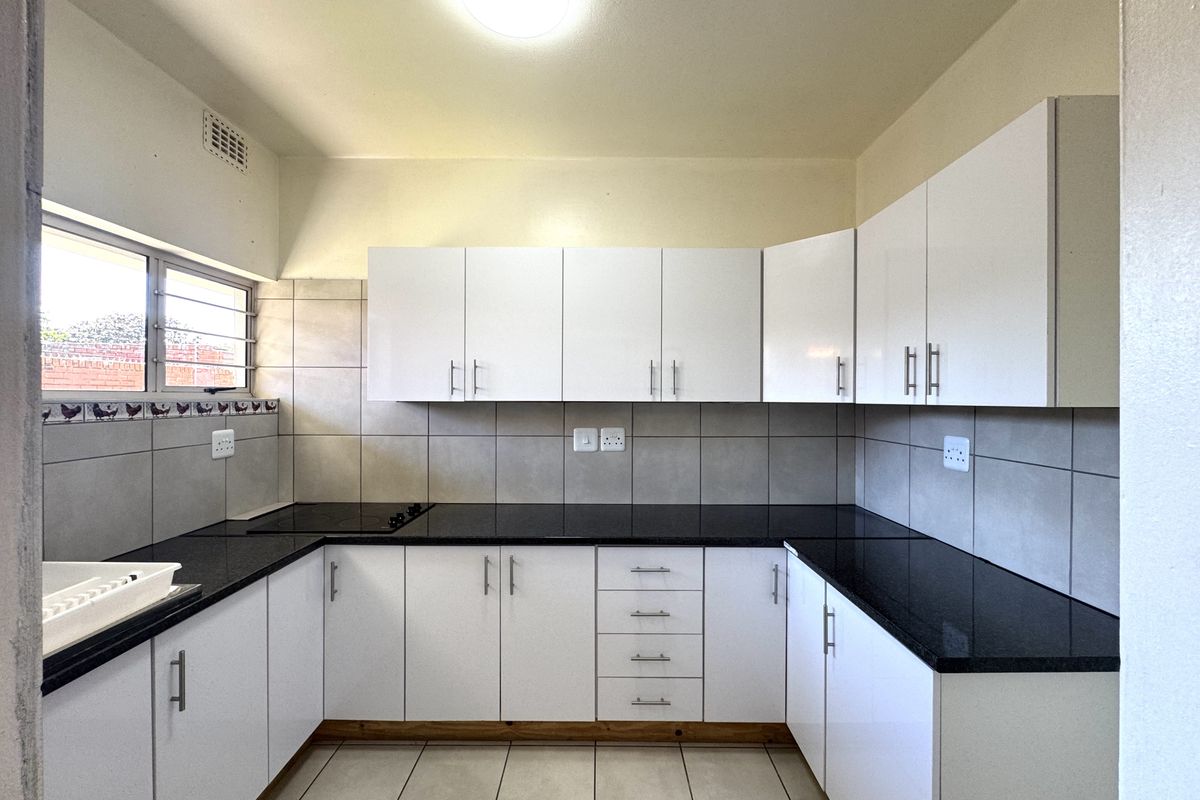A clean, modern kitchen featuring white cabinetry, dark granite countertops, tiled splashbacks, and a built-in electric hob.