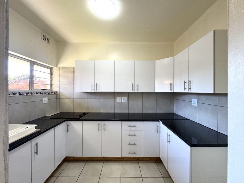 A clean, modern kitchen featuring white cabinetry, dark granite countertops, tiled splashbacks, and a built-in electric hob.