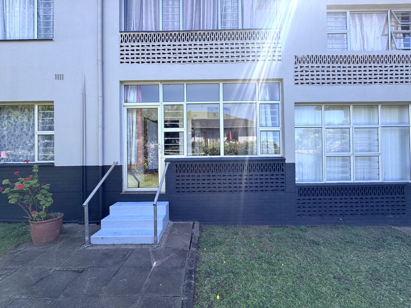 Rear exterior view of the flat featuring a paved patio, concrete steps with handrail, and decorative breeze block architectural detailing.