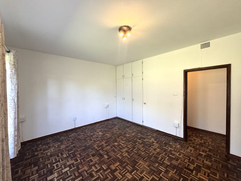 A spacious, empty bedroom featuring classic parquet flooring, built-in storage cupboards, and neutral wall finishes, ready for personalization.