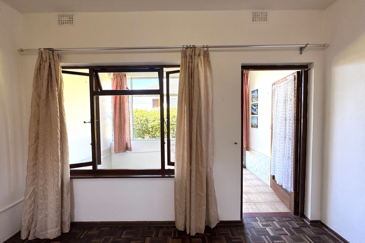 A vacant bedroom featuring classic parquet flooring, timber window frames, and direct access to an adjoining sunroom or balcony area.