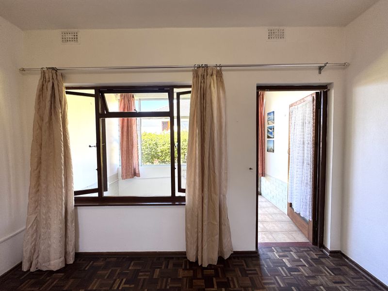 A vacant bedroom featuring classic parquet flooring, timber window frames, and direct access to an adjoining sunroom or balcony area.