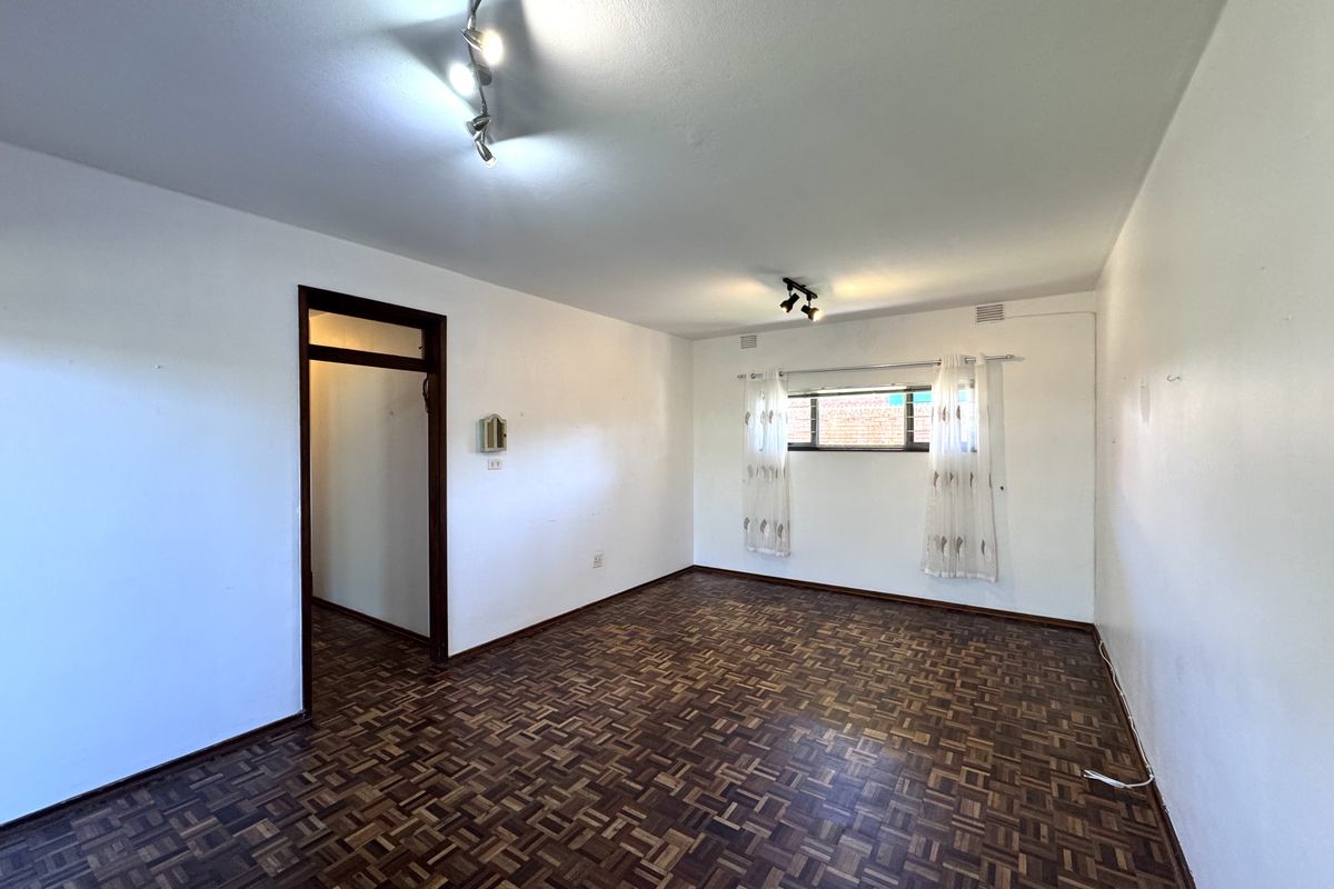 A spacious, empty living room featuring classic parquet flooring, neutral white walls, and modern track lighting, offering a versatile blank canvas.