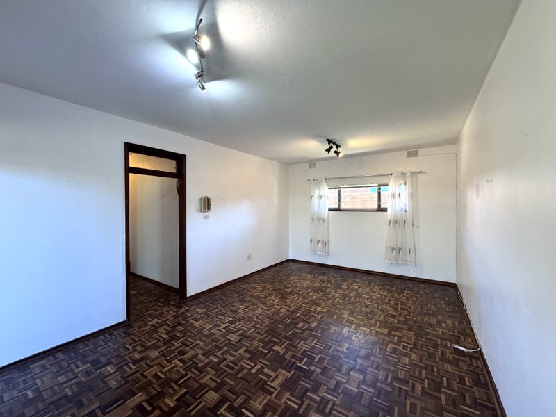 A spacious, empty living room featuring classic parquet flooring, neutral white walls, and modern track lighting, offering a versatile blank canvas.