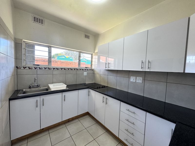 A clean and functional kitchen featuring white cabinetry, black granite countertops, ceramic tile flooring, and a built-in hob.
