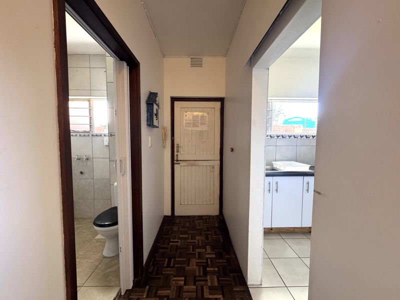 A central hallway featuring parquet flooring, providing access to an adjacent bathroom and kitchen area.
