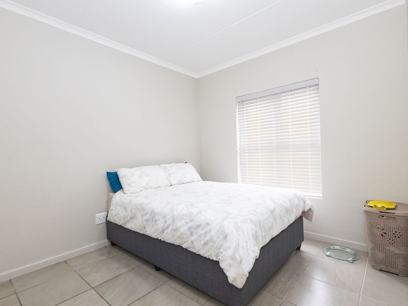 A clean and neutral bedroom featuring tiled flooring, coved ceilings, and a window fitted with venetian blinds.
