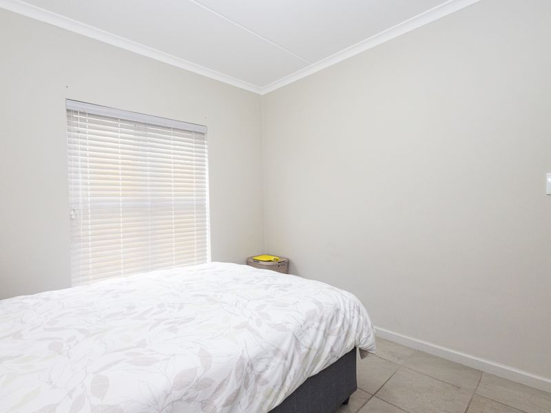 A clean and neutral bedroom featuring tiled flooring, white walls, and venetian blinds, offering a blank canvas for personalization.