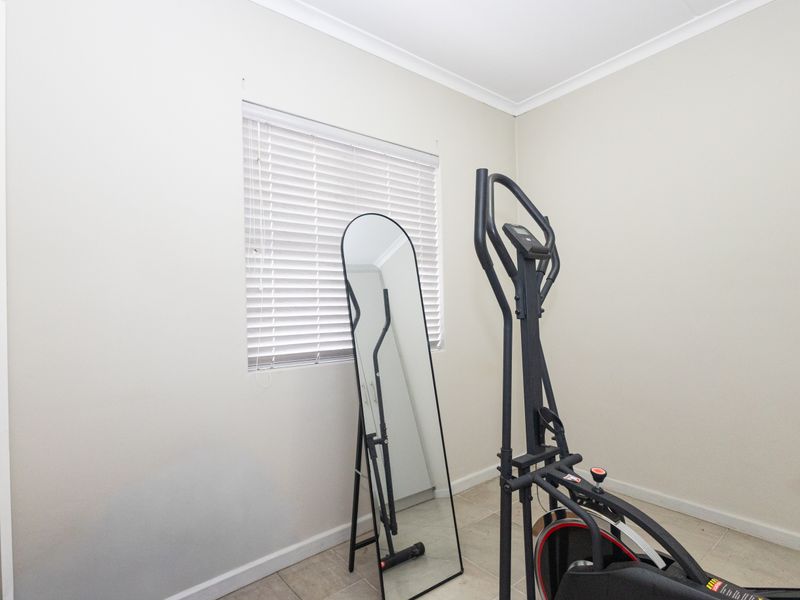 A neutral-toned bedroom featuring tiled flooring, cove cornicing, and a window fitted with venetian blinds, offering a clean and versatile living space.