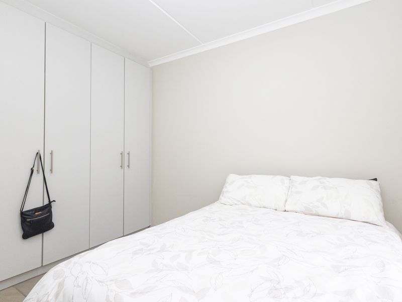 A clean and neutral bedroom featuring ample built-in cupboard storage and a simple, modern aesthetic.