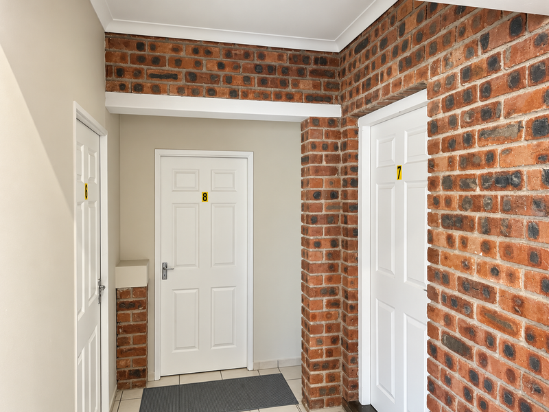 A clean, well-maintained hallway featuring exposed brick accents, tiled flooring, and multiple numbered panelled doors.