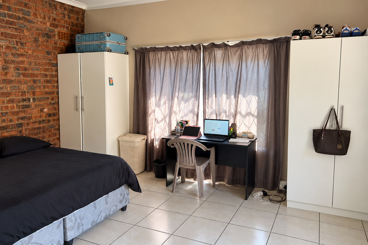 A bedroom featuring an exposed brick feature wall, ceramic tiled flooring, and built-in storage cupboards.