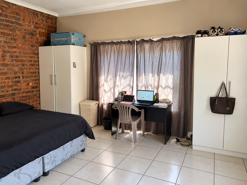 A bedroom featuring an exposed brick feature wall, ceramic tiled flooring, and built-in storage cupboards.