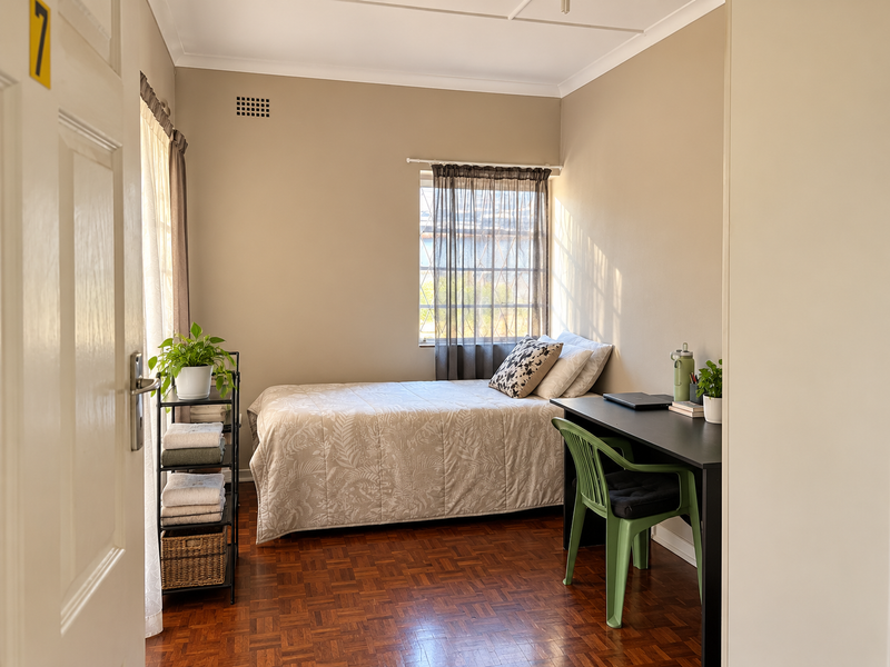 A compact bedroom featuring warm parquet flooring, neutral wall tones, and a window fitted with a security gate for added peace of mind.