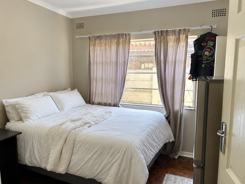 A bedroom featuring parquet flooring, neutral wall paint, and a window fitted with security bars.