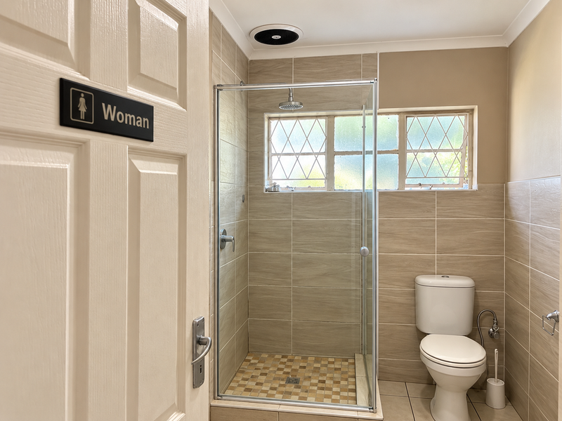 A clean, functional bathroom featuring a glass-enclosed shower, tiled walls, and a standard toilet, finished with neutral tones and leaded glass windows.