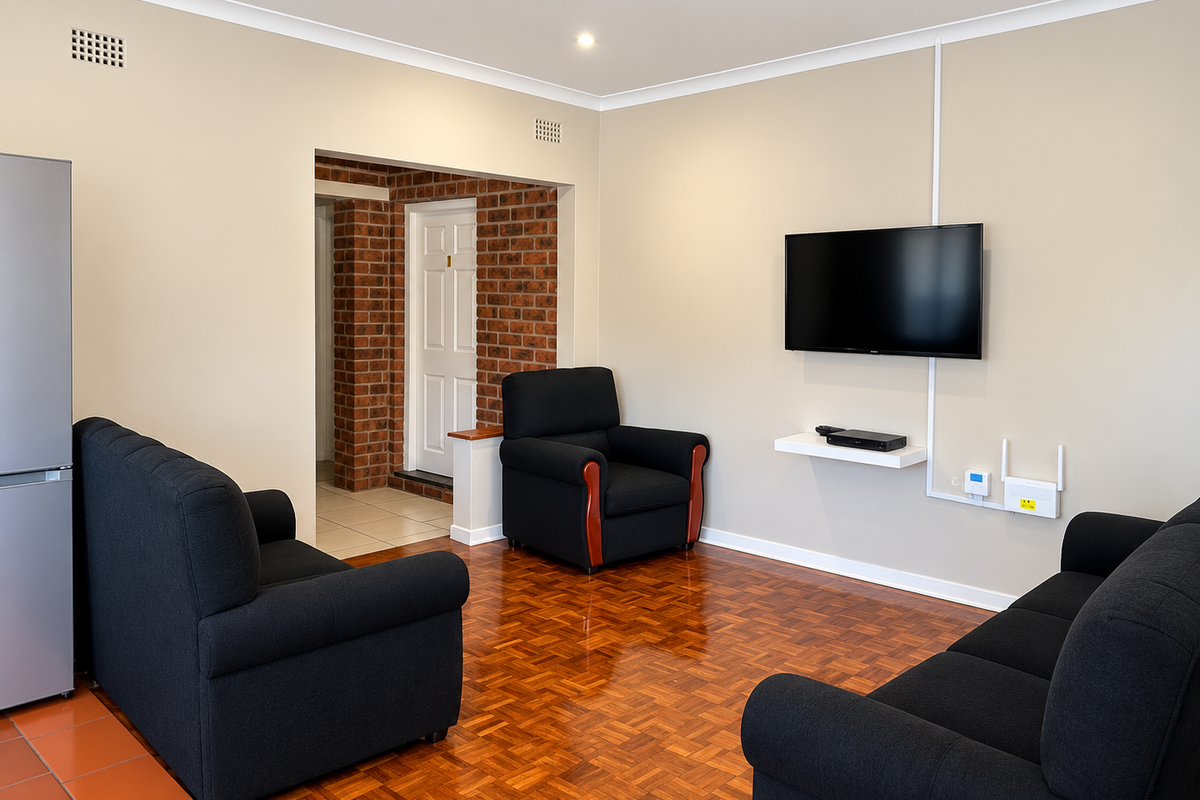 A living room featuring polished parquet flooring, recessed downlights, and an exposed brick feature wall leading to an adjacent hallway.