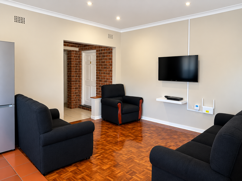 A living room featuring polished parquet flooring, recessed downlights, and an exposed brick feature wall leading to an adjacent hallway.