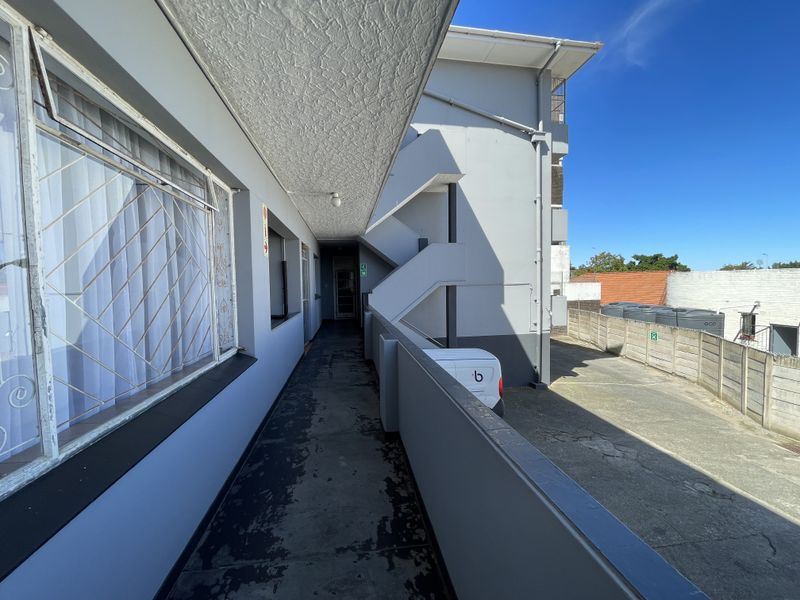 An exterior apartment walkway featuring a concrete floor with visible wear, security bars on windows, and an adjacent staircase.