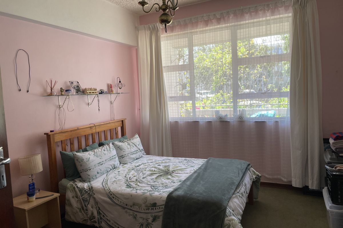 A bedroom featuring a large window with security bars and a classic ceiling light fixture, requiring cosmetic updates to the wall finishes and flooring.