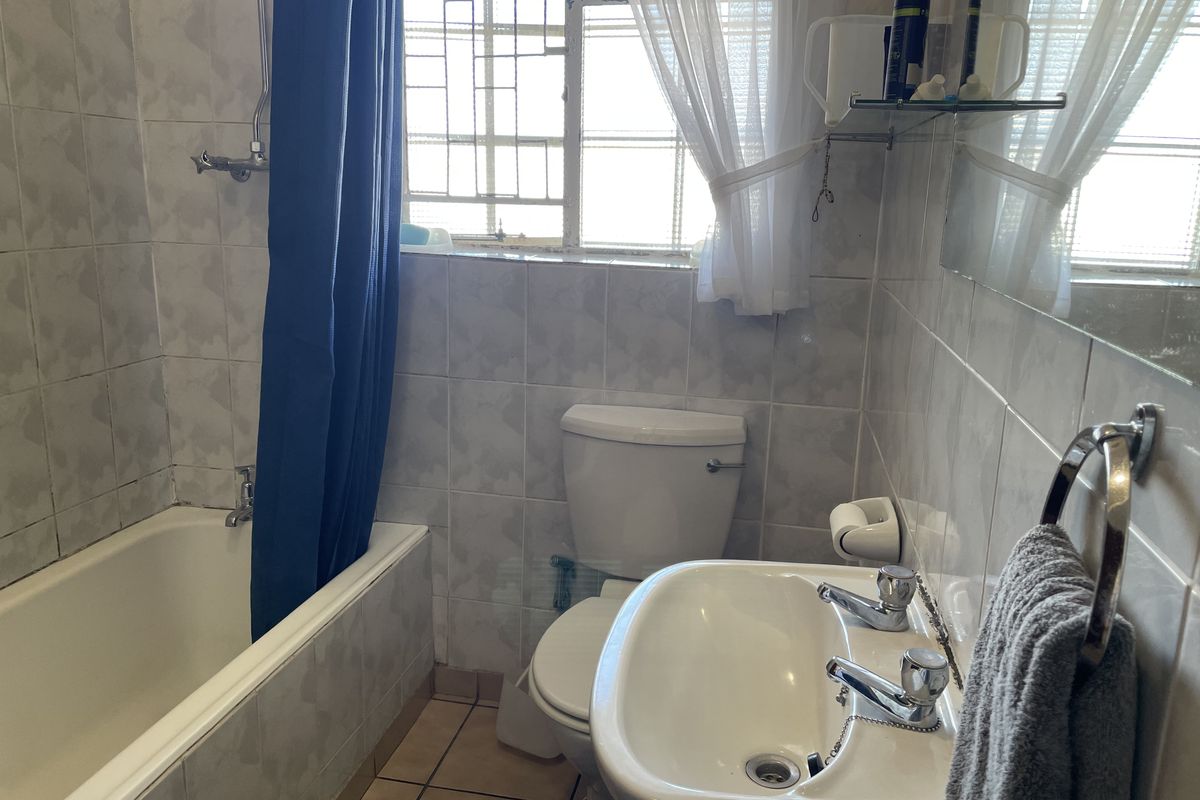 A functional bathroom featuring a bathtub with shower mixer, pedestal basin, and toilet, finished with neutral wall and floor tiles.