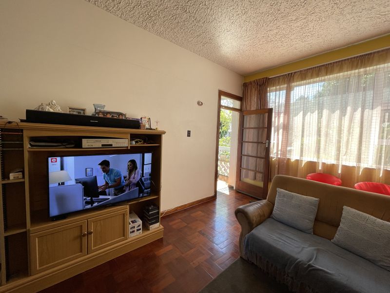 A living room featuring classic parquet flooring, a textured ceiling, and a timber-framed glass door providing access to an outdoor area.