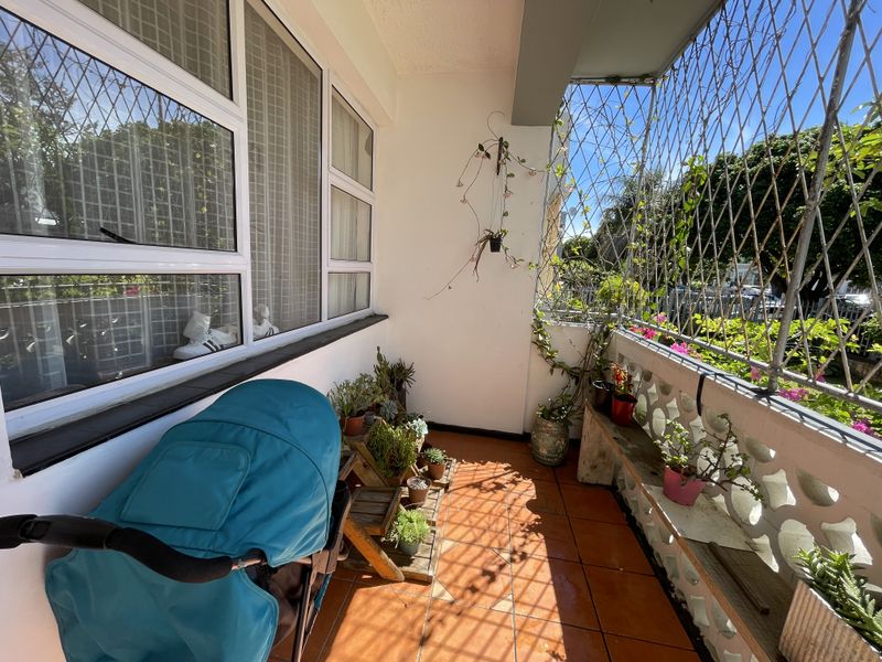 A sunny balcony featuring tiled flooring, a decorative concrete screen wall, and security mesh, offering a bright outdoor space for relaxation.