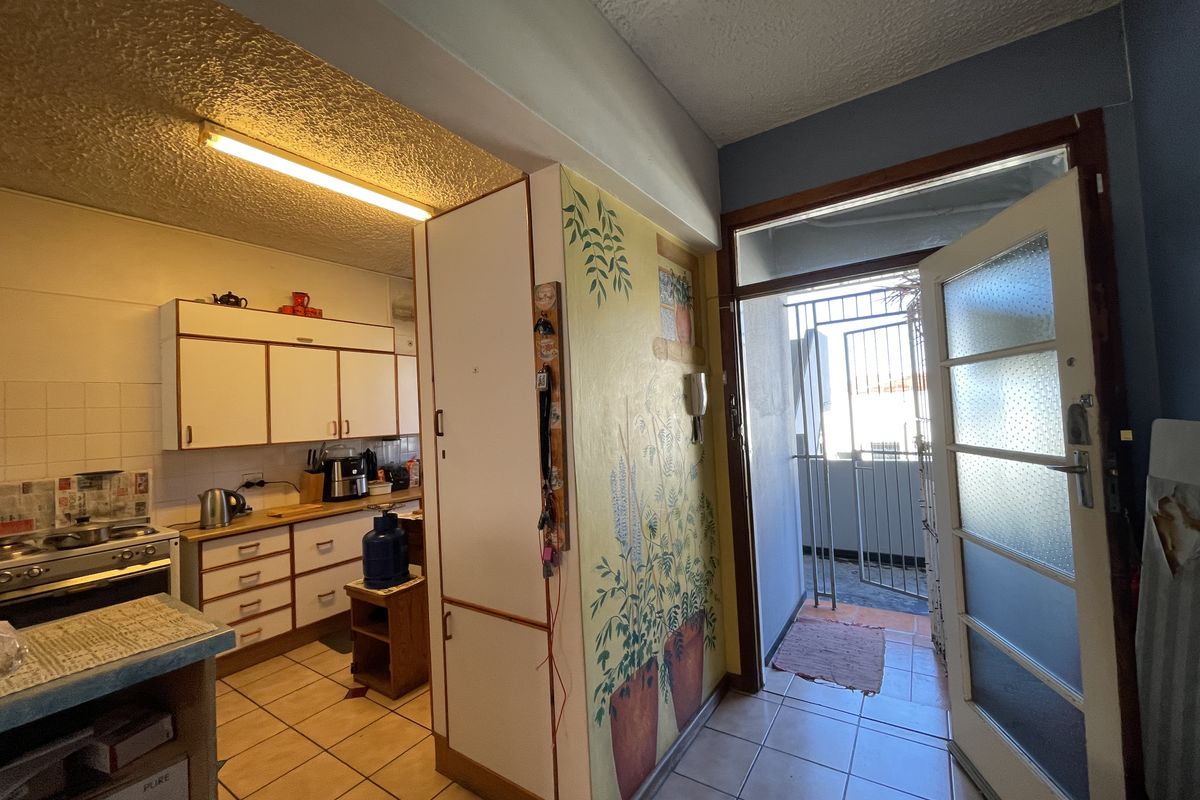 A functional kitchen area featuring built-in cabinetry and a gas stove, with direct access to an exterior security gate and tiled flooring throughout.