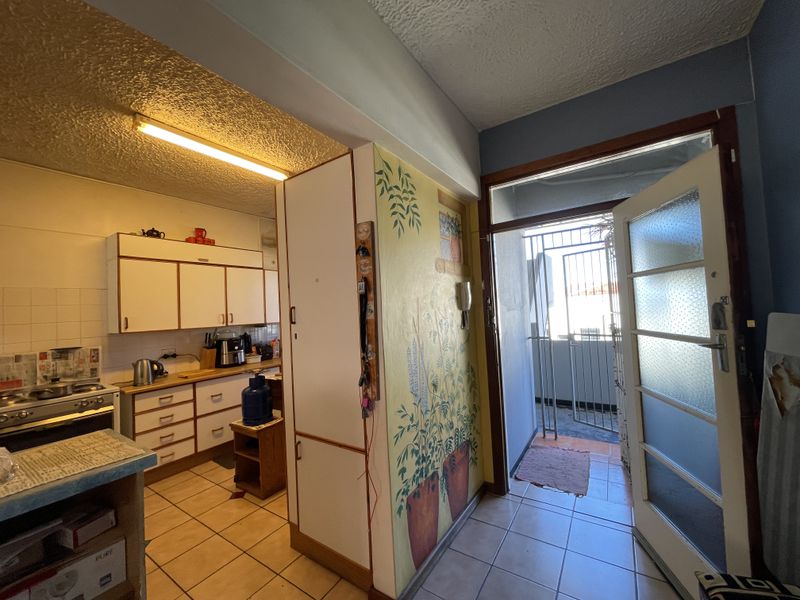 A functional kitchen area featuring built-in cabinetry and a gas stove, with direct access to an exterior security gate and tiled flooring throughout.