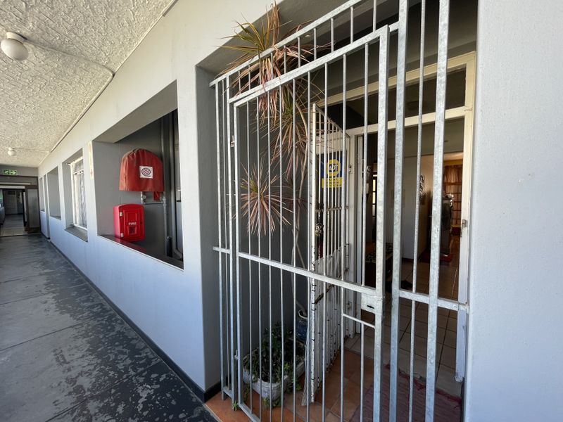 Apartment entrance featuring a security gate, with communal walkway access including fire safety equipment.