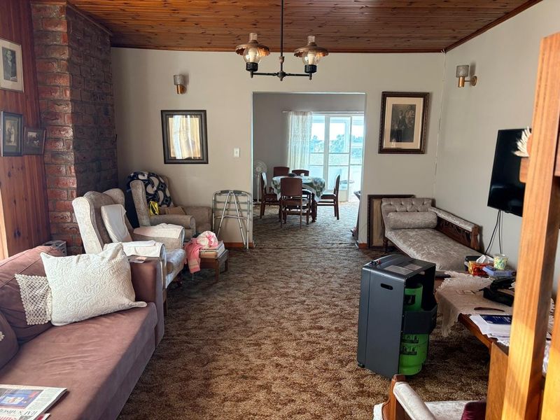 Open plan living and dining area featuring an exposed brick fireplace and timber ceiling, offering a traditional layout with potential for modern updates.