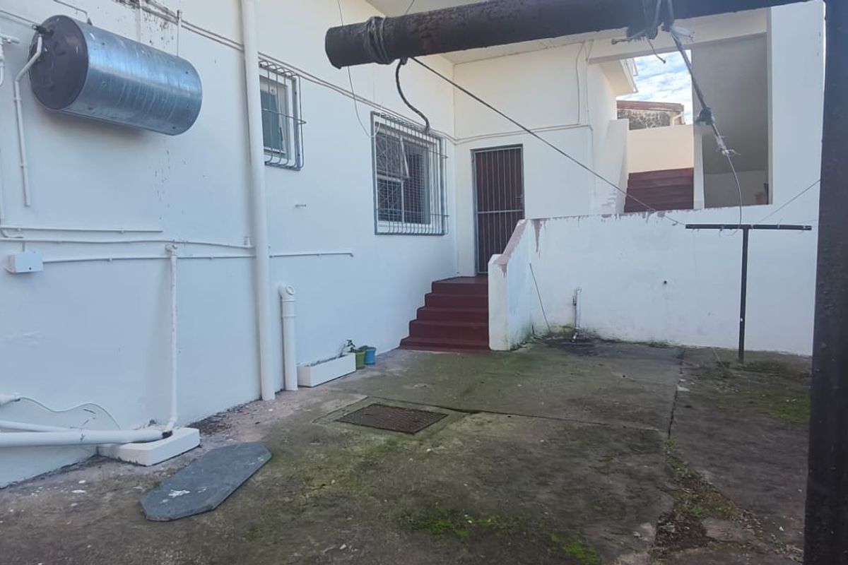 Rear exterior area featuring concrete paving, an external staircase, and an externally mounted electric water heater on the building facade.