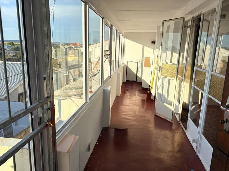 An enclosed balcony featuring large glass windows, providing an airy space with potential for a sunroom or seating area.