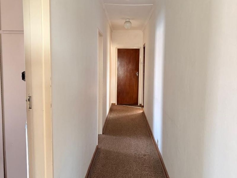 A narrow residential hallway featuring carpeted flooring and simple interior doors, providing access to various rooms within the home.